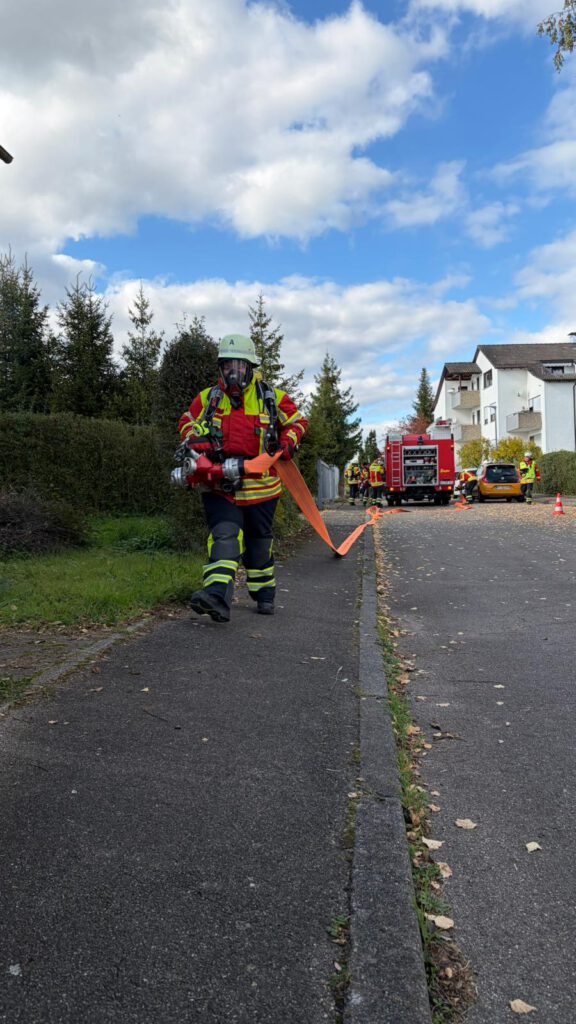 Eine Person des Angriffstrupps bringt den Schnellangriffsverteiler in Stellung.
Auf dem Bild läuft eine Person mit Atemschutzmaske und hält einen Verteiler in der Hand. An diesem Verteiler ist ein B-Schlauch angekuppelt, welcher gleichzeitig durch das gehen ausgerollt wird.